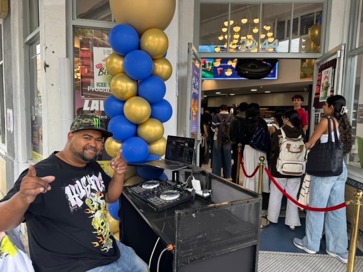 A DJ and balloon arch at a restaurant entrance with a line of guests filing in
