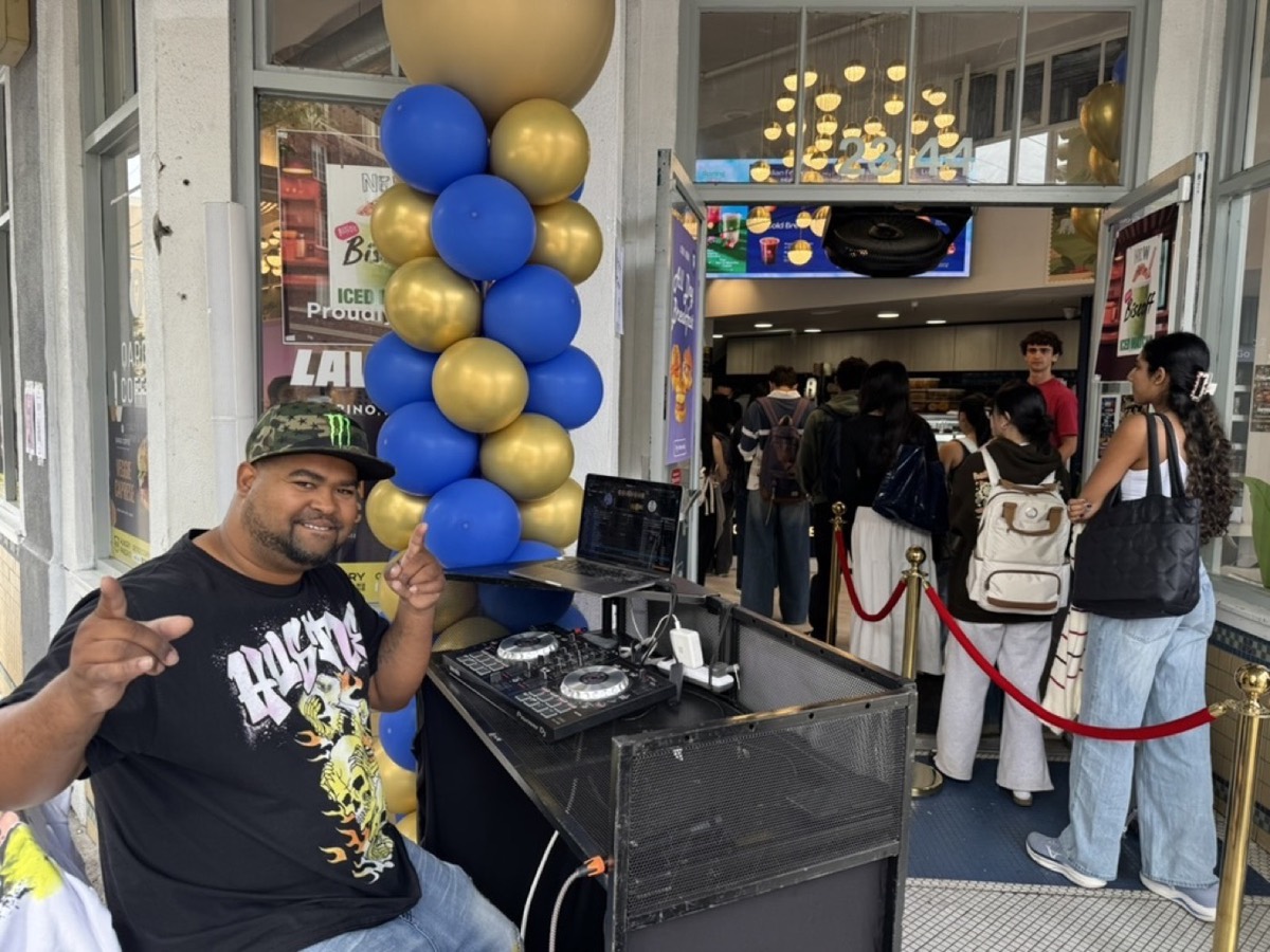 A DJ and balloon arch at a restaurant entrance with a line of guests filing in